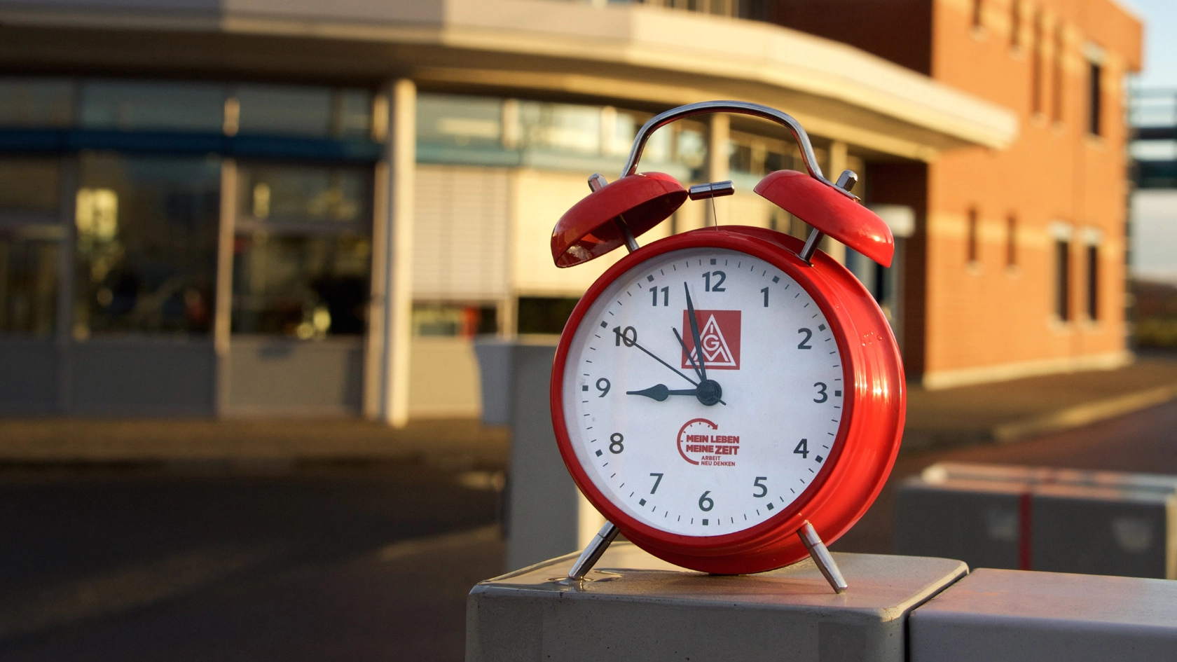 Ein roter Wecker vor einem Industriegebäude.