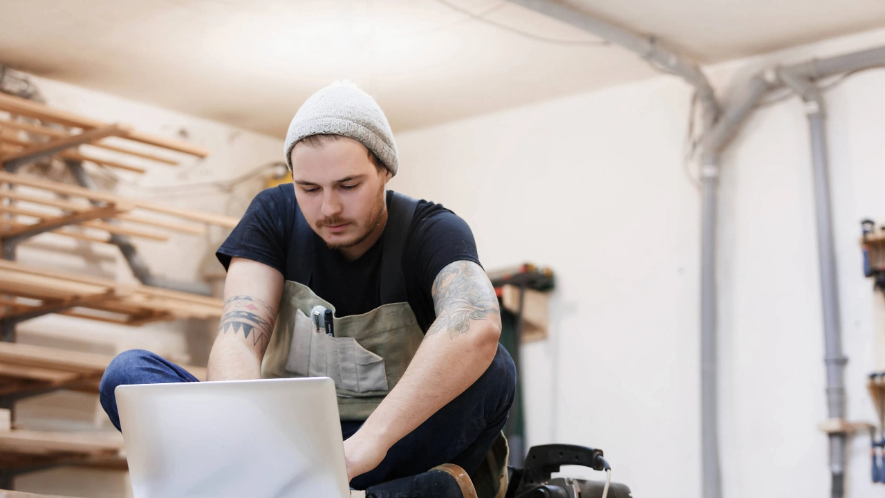 Ein junger Mann in einer Werkstatt blickt in ein Notebook.