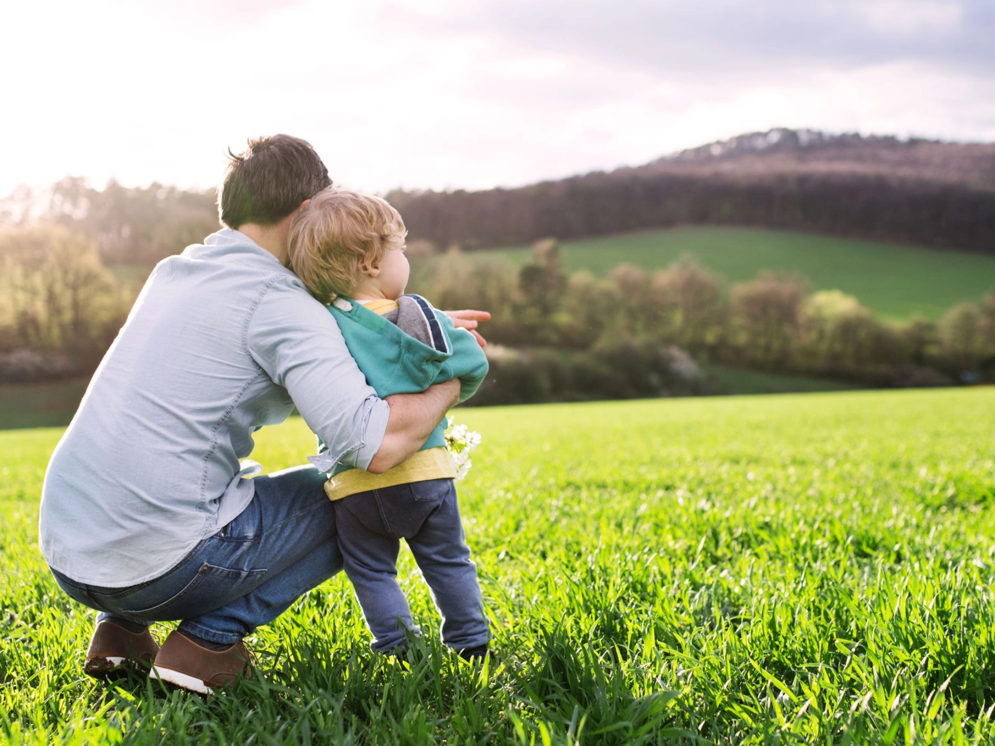 ein Vater schaut mit seinem Kind über eine grüne Landschaft